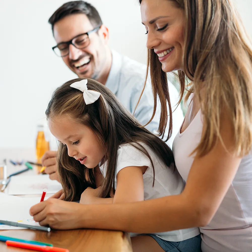 A laughing mother and father helping their child write in a book at a Little Sprouts daycare