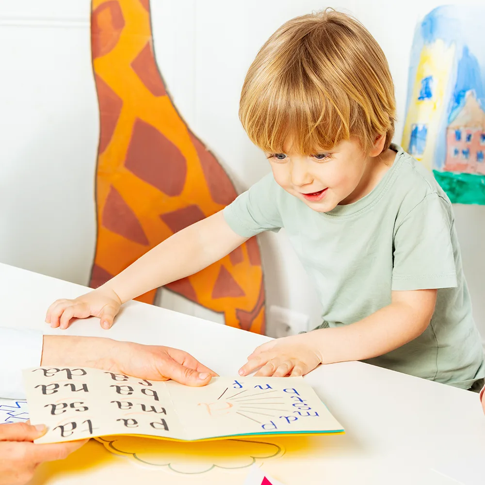 A child smiling and looking at a school book at a Little Sprouts daycare