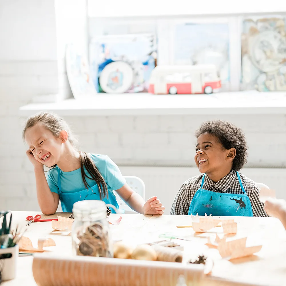 Two children laughing at a table working on crafts at a Little Sprouts daycare