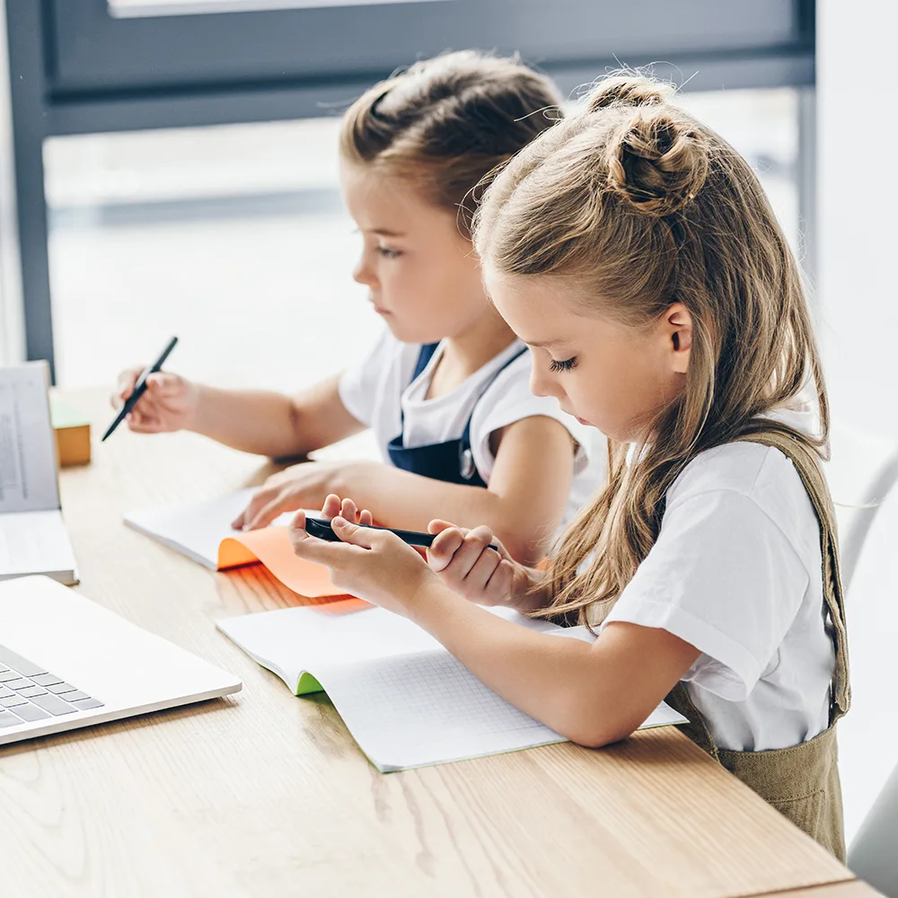 Two children working with pens and a laptop at a table in a Little Sprouts daycare