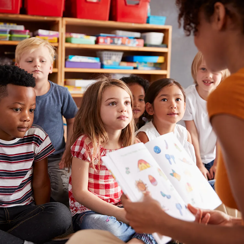 Children listening to a teacher read from a picture book at a Little Sprouts daycare