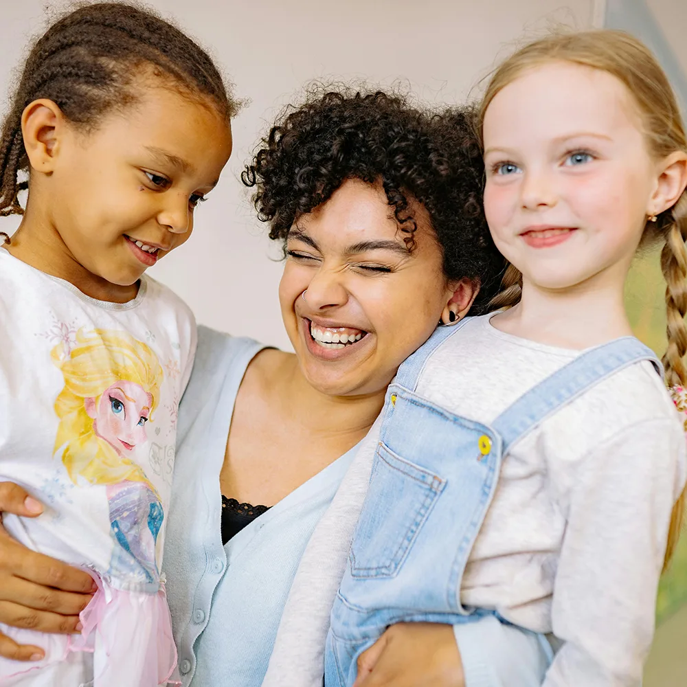 An adult hugging two children and smiling at a Little Sprouts daycare