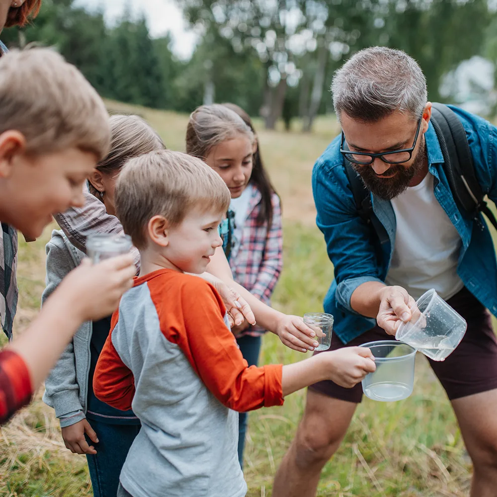 An adult playing with kids and glasses of water outside of a Little Sprouts daycare