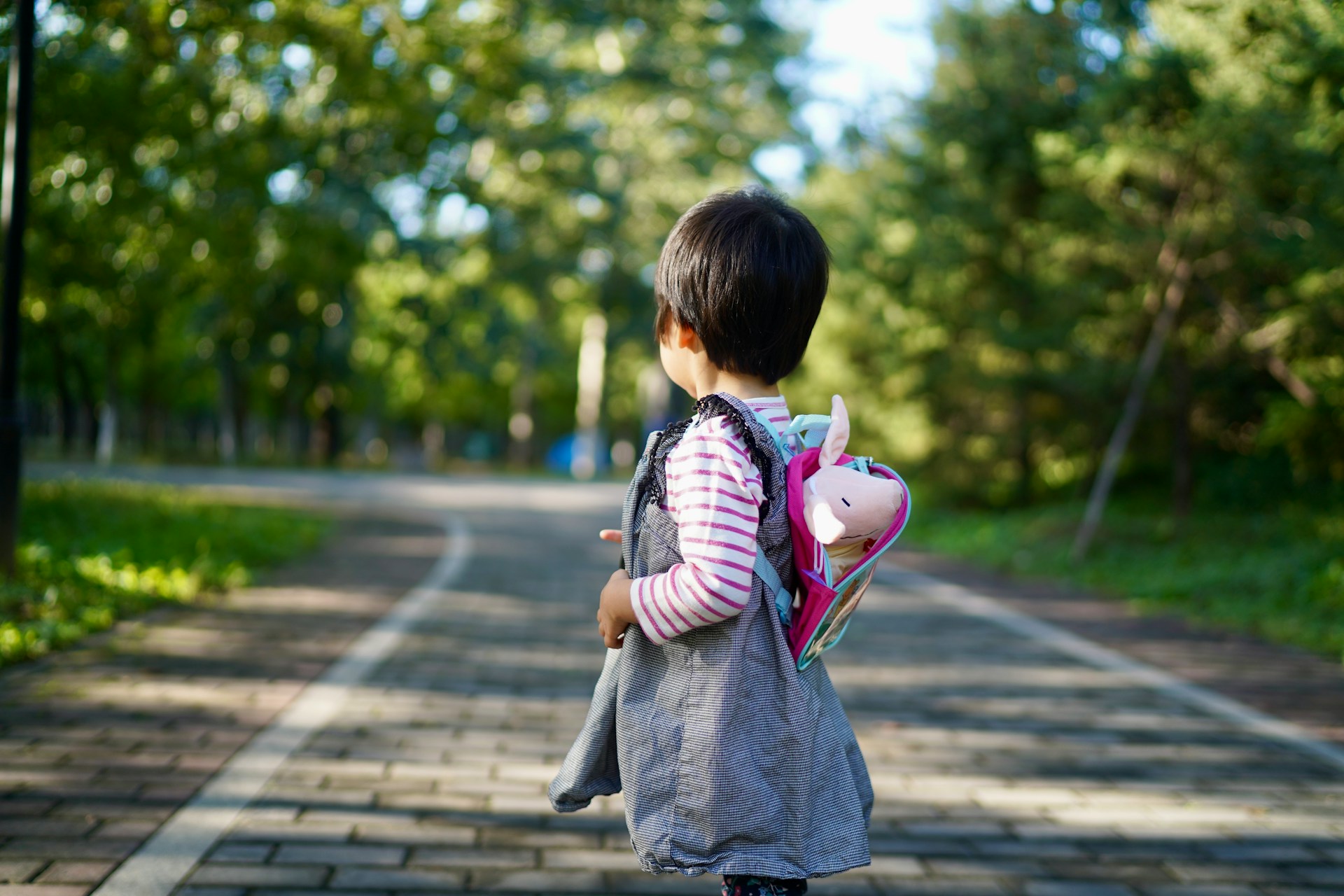 A young child with a backpack walks on a path